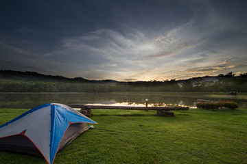 Camping tent on green grass beside lake with foggy over forest during sunrise, Thailand