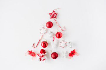creative arrangement of bright red christmas tree made of christmas ball, sweets, toys on white background. flat lay, top view