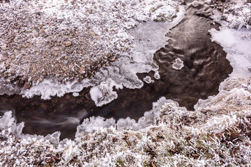 Winter Creek bed. Creek that flows in the creek bed, covered of snow in winter and the ice coast.