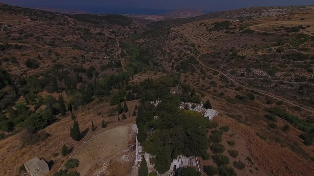 Aerial shot of Greek village in mountains, starting with small cemetery, pulling back to reveal unique church and houses of this idyllic town.