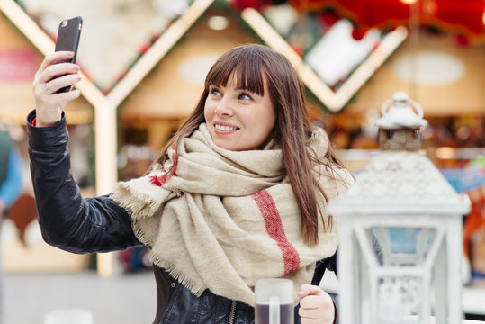 beautiful woman drinks mulled wine and makes a selfy on mobile p