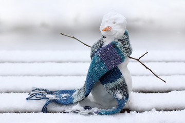 good mood during the winter holidays/ Christmas snowman in a warm scarf on the background of snowy...