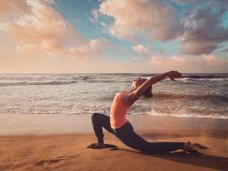Fototapeta na wymiar Sporty fit woman practices yoga Anjaneyasana at beach on sunset