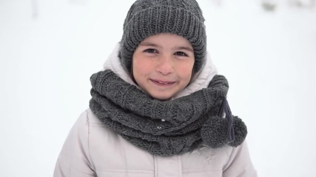 Portrait of a smiling kid girl wearing in grey hat and scarf outdoor in winter time