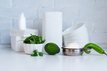 Cooking concept, kitchen interior - mushrooms. salad, green herbs, avocado, bowl of flour, green chili pepper pod, oil jug and dishes on white against white brick wall. Copy space.