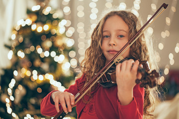 Young girl playing violin in front of christmas tree