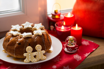 Christmas decoration: cake, gingerbread-men and burning red candles on windowsill