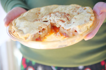 A man holds a homemade apple pie sprinkled with cinnamon.