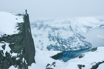 Alone man standing over majestic landscape covered by snow with deep valley and big sharp mountains...
