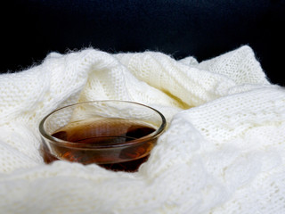 Glass cup of hot tea, dressed in knitted warm scarf winter warm knitted sweater or blanket. Still scarf and a cup of tea with Christmas tree. In the winter time. Cozy and soft winter background.