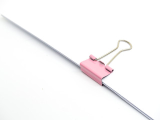 Pink paperclip attached on white paper isolated
