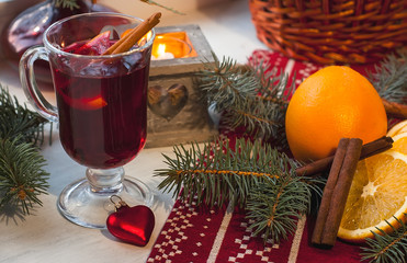 Glass of hot mulled wine on wooden table with candle, orange, cinnamon and christmas tree. Winter...