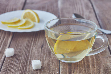 Glass cup of green tea and sliced lemon on wooden background