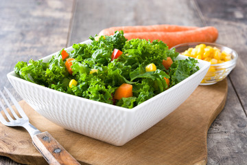 Kale salad in bowl with carrot, pepper and sweet corn on wooden background
