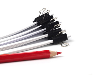 red pencil in front of several stacks of paper held by binder clips, shallow depth of field