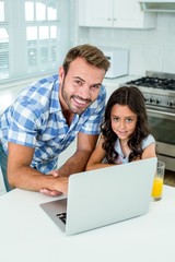 Happy man with daughter using laptop in kitchen