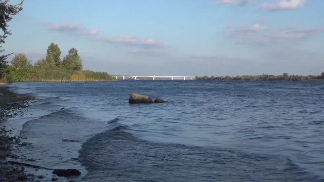 Walk along the Dnieper River, near the bridge.  Morning, quiet water in the foreground rocks and picturesque vegetation. The sunset moment. Attracted waves. Expressive long-range plan.