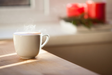 A cup of coffee on table and red blurred candles on background

