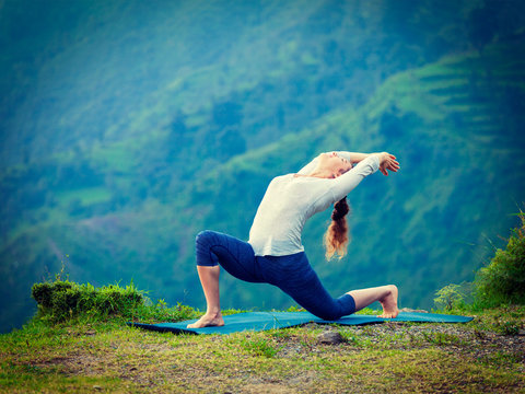 Sporty fit woman practices yoga asana Anjaneyasana in mountains
