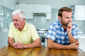 Tensed father and son sitting at table in kitchen