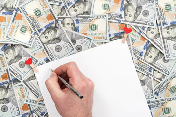 Men hand writes a pen on a blank sheet, lying on a pile of dollars