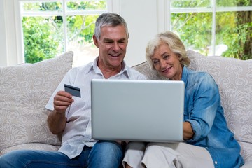 Senior couple shopping online using laptop at sitting room