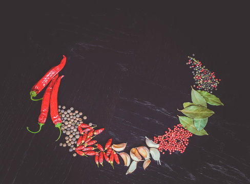 Frame of spicy background with assortment of different hot chilies, allspice, brazilian peppers, garlic and bay leaves over rusty black wooden background. Top view. 