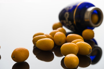 pile of fresh bright yellow kumquat on black glass desk with blue glass bottle