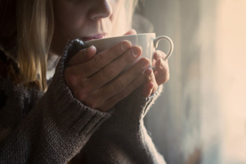 Woman in knitted sweater hands holding a cup of warm coffee