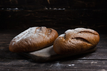 Two black bread with flour on a wooden background. Advertising bread. Leaning flour.