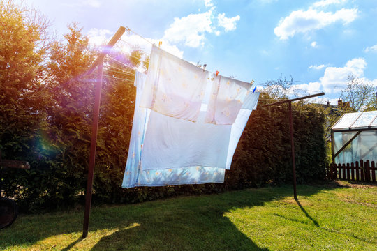 laundry drying.Sheet hanging on clothesline in front of blue sky and sun.White clean sheets outdoors.