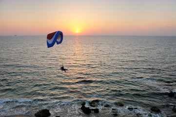 Powered paraglider flying over the sea at sunset sky background