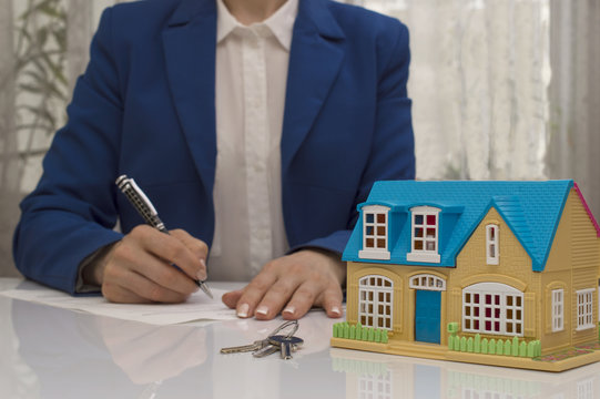 woman with house model and pen signing contract document
