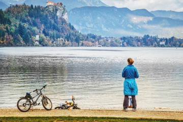 Family recreation at Bled lake in Slovenia. Beautiful landscape with Alps at background and mother with child, outdoor sport family activity with bicycle at pond seafront. Rear view.