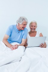 Happy senior couple using laptop while sitting on bed 