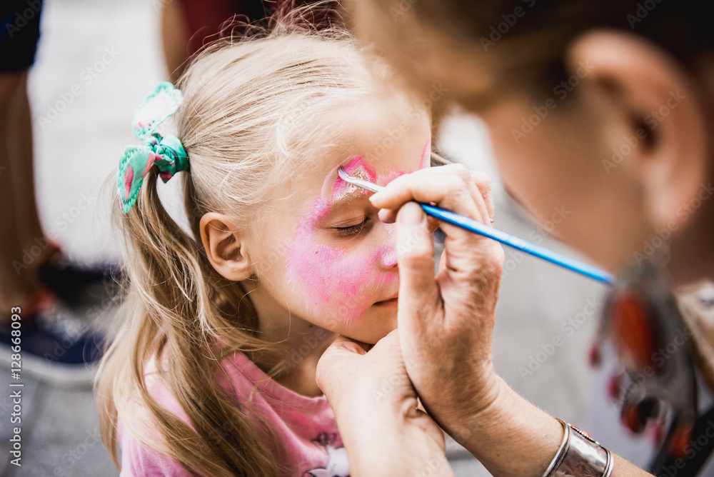 Wall mural woman painting face of kid outdoors