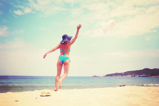 Woman in blue bikini throwing her hat on the beach
