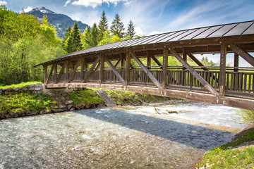 Überdachte Holzbrücke quert einen Wildbach im Gebirge