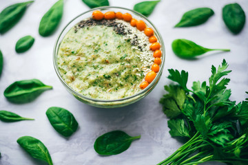 green smoothie with sea buckthorn, Chia seeds and sesame seeds on a white table, around spinach leaves and a bunch of parsley. The concept of healthy eating, vegetarian and vegan food, top view