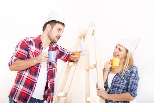 Young smilling couple painting wall in their new house. Home, moving, painting and renovating concept