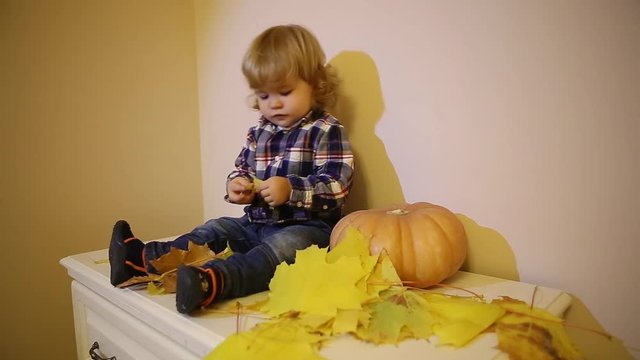 Cute baby boy with pumpkin playing with leaves halloween