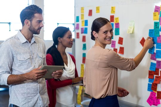 Team Of Colleagues Standing By White Board Reading Sticky Notes