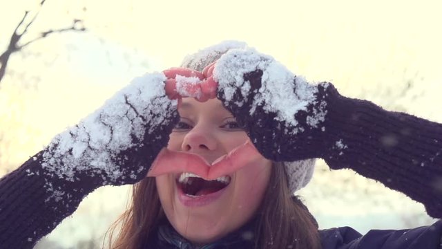 Winter girl showing heart sign. Joyful teenage model girl having fun in winter park. 1080p. 240 fps