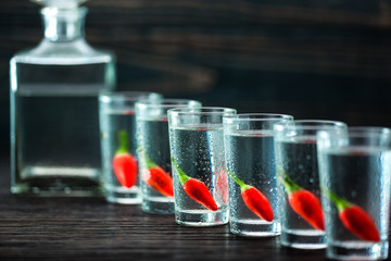 vodka with  peppers on wooden table, selective focus
