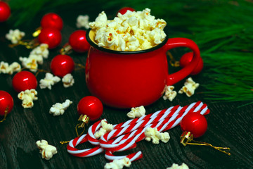 Salty fresh crusty homemade popcorn in red cup in the fashion black background in a New Year's interior with red Christmas balls.