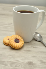 A white mug with coffee and round jam filled biscuits