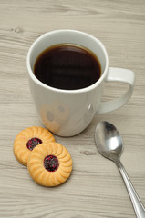 A white mug with coffee and round jam filled biscuits