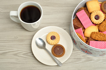 Cup of coffee with a tin filled with biscuits