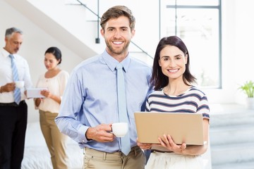 Fototapeta premium Businessman holding coffee cup and a colleague holding laptop
