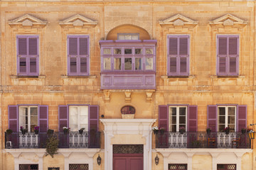 Front view of a medieval Mediterranean style building with purple balcony, windows and shutters 